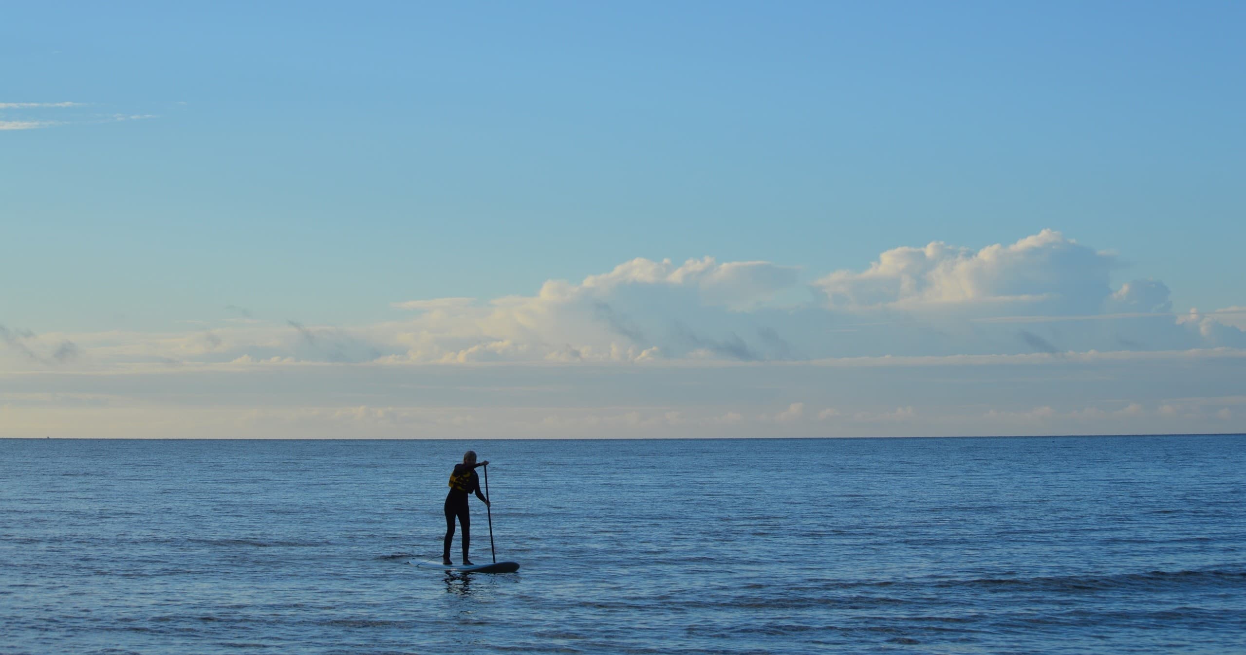 Standup paddleboarder silhouette on calm coastal ocean at dusk