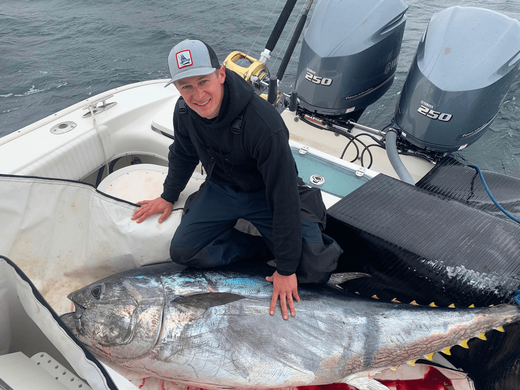 Sportfisher kneeling beside giant yellowfin tuna on deck, boat