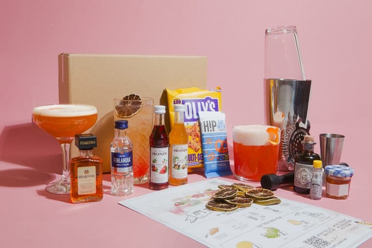 Assorted cocktail ingredients and tools on pink studio backdrop