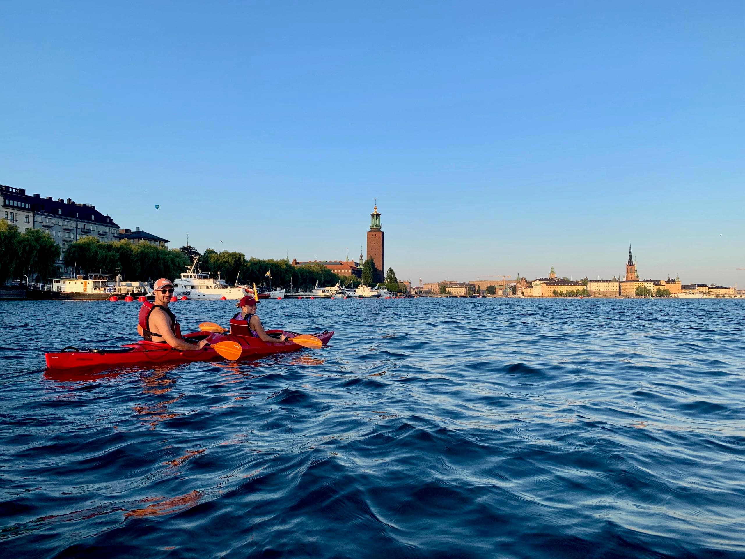 Red kayak paddling along Stockholm waterfront with city hall