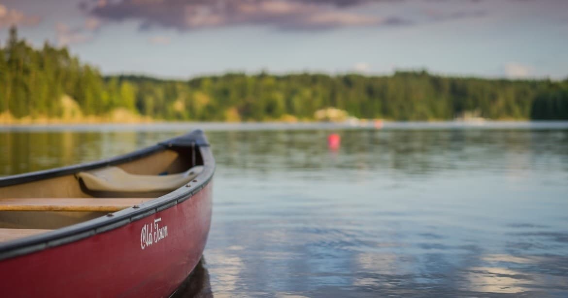 Red canoe drifting on a calm forest lake at sunrise, serene