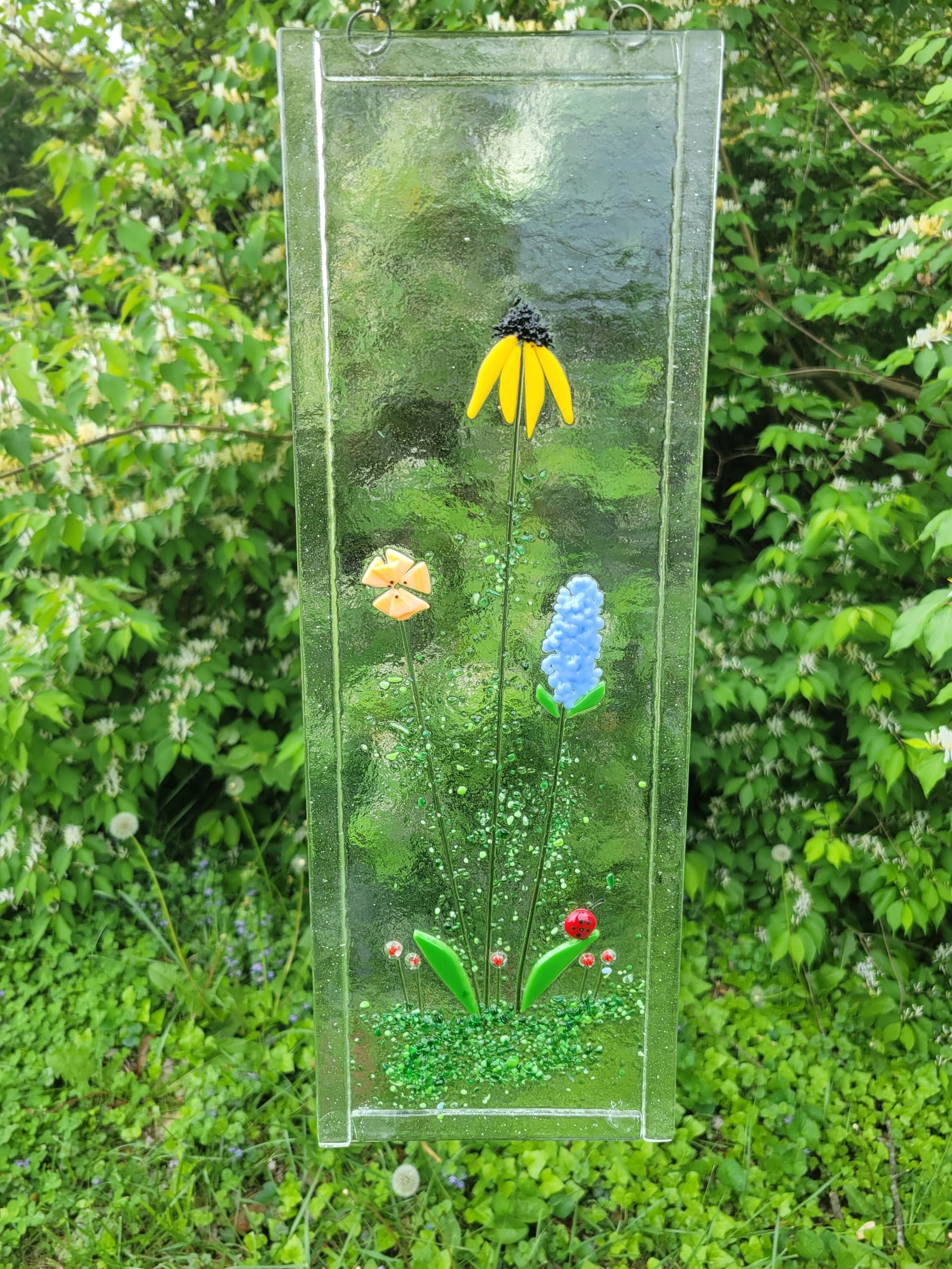 Tall fused glass garden panel with flowers installed outdoors