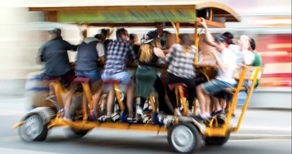 Pedal trolley group tour on urban street, people pedaling and socializing