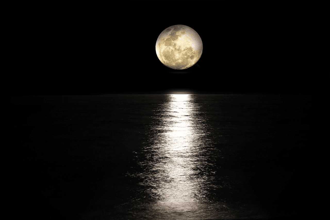 Full moon reflecting on calm ocean at night over horizon