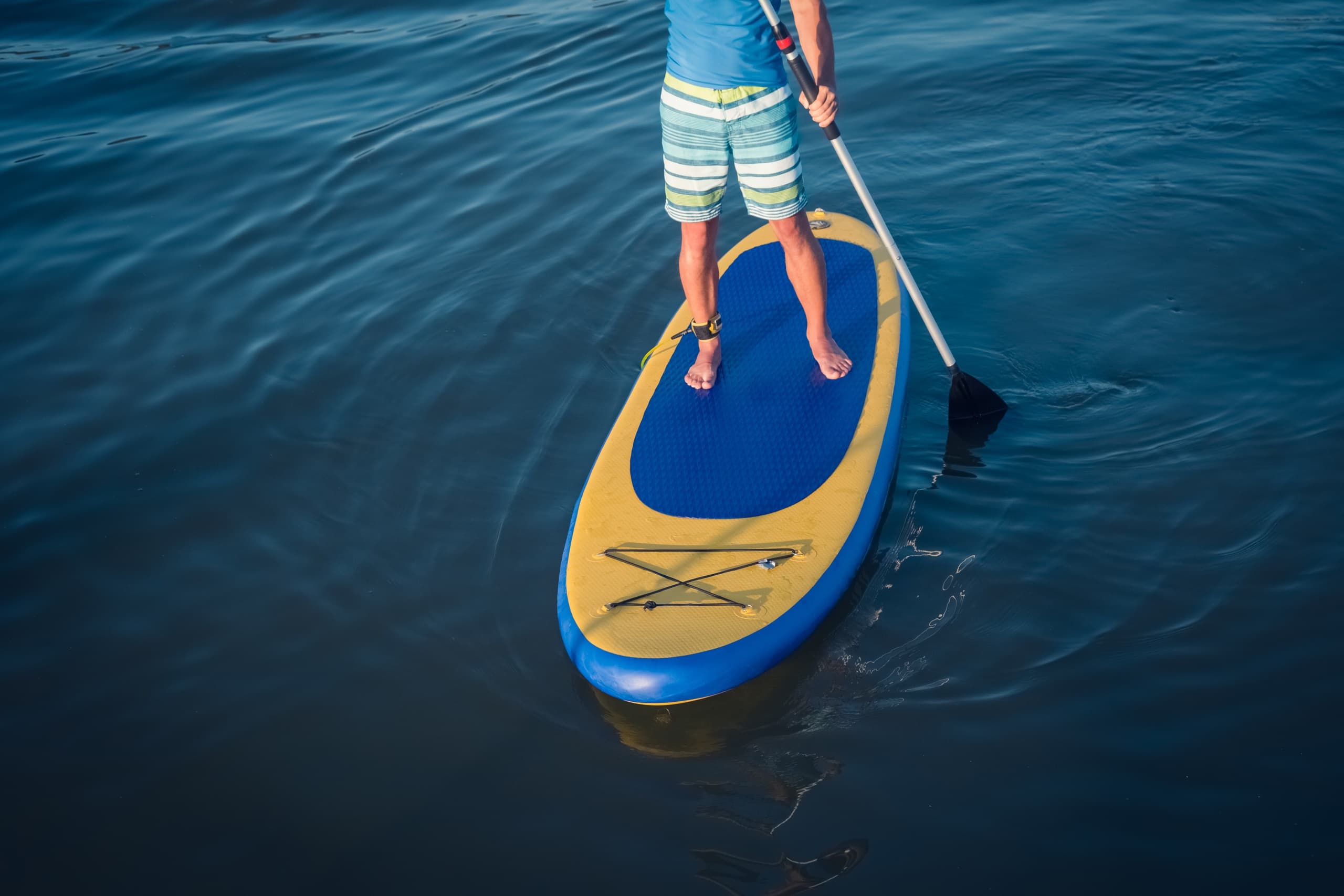 Stand-up paddleboarder paddling on calm blue lake near shore