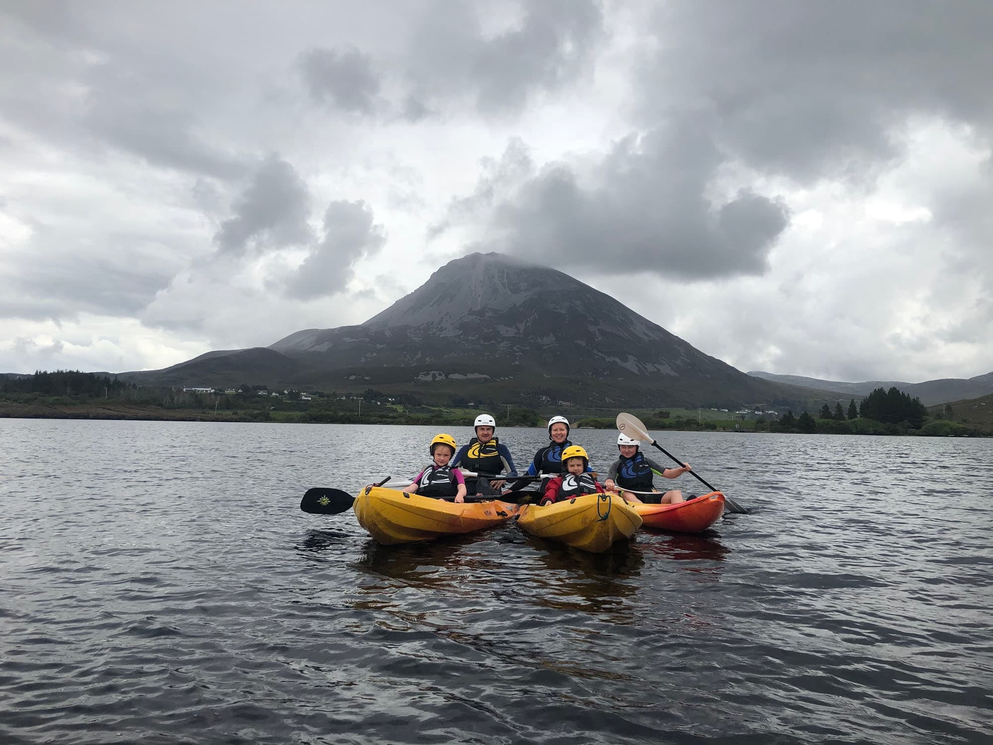 Guided kayakers paddling near mountain on overcast lake
