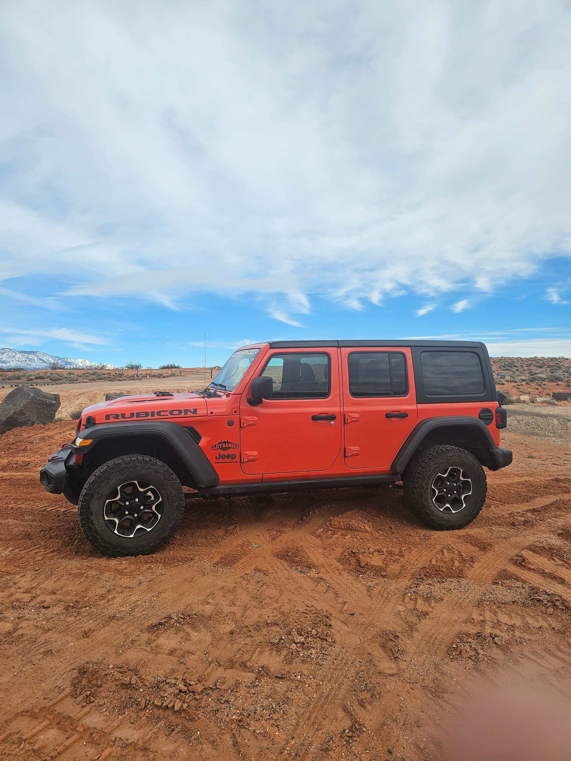 Orange Jeep Rubicon off-roading on red desert sandstone trail