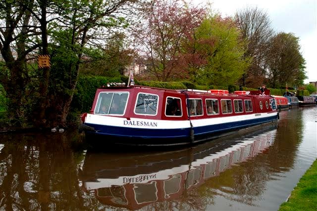 Canal boat reflected in calm towpath water under trees