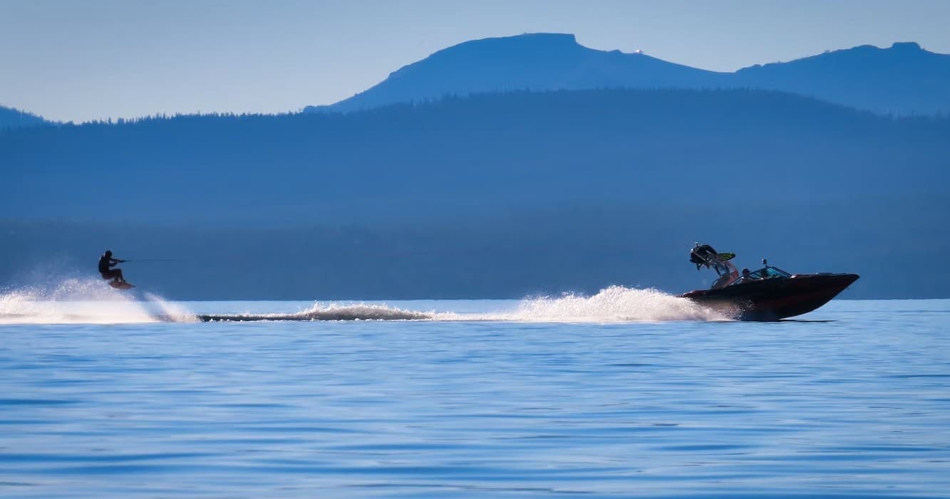 Waterskier towed behind boat on alpine lake with mountain backdrop