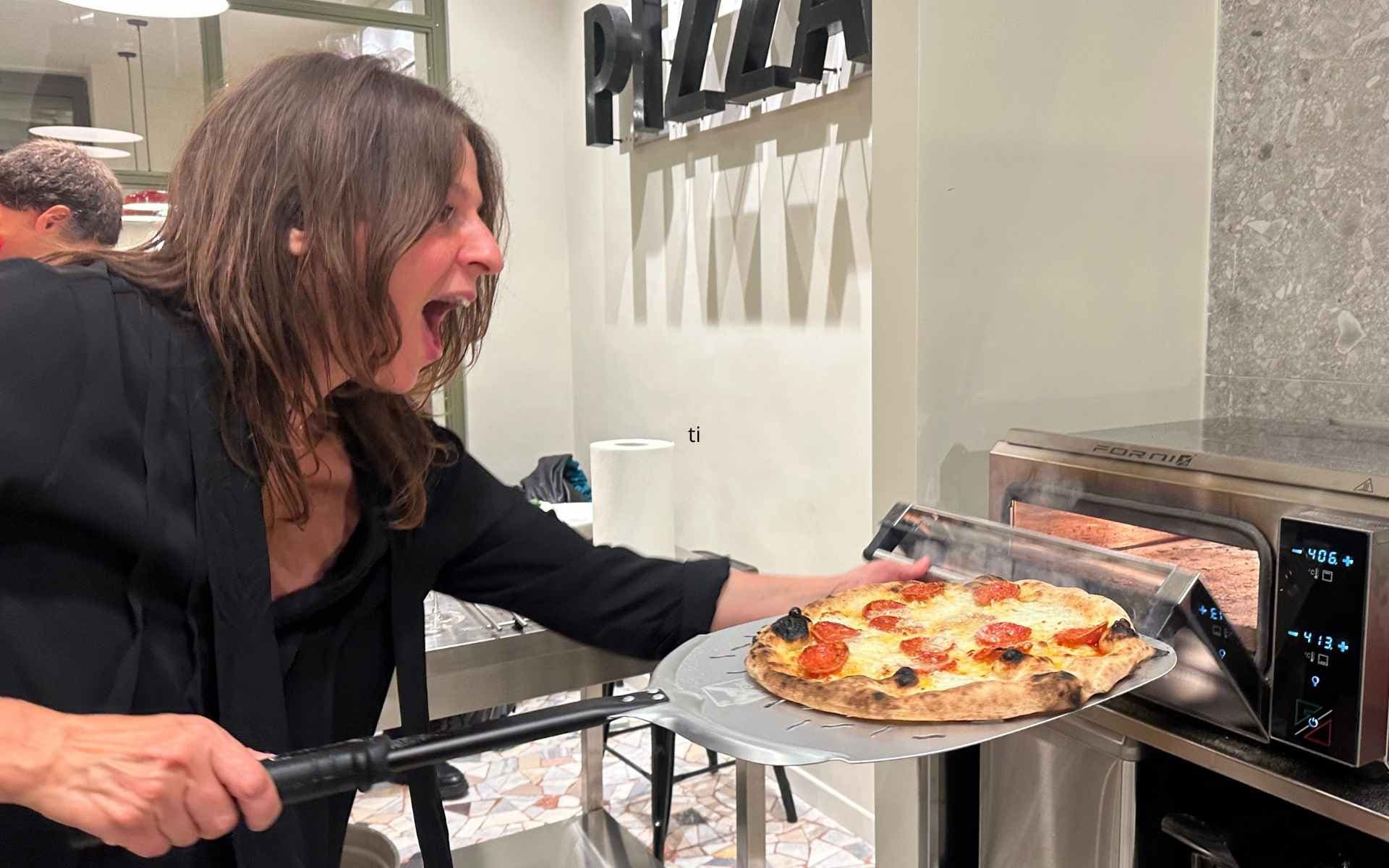Guest removing wood-fired pizza during pizza-making class