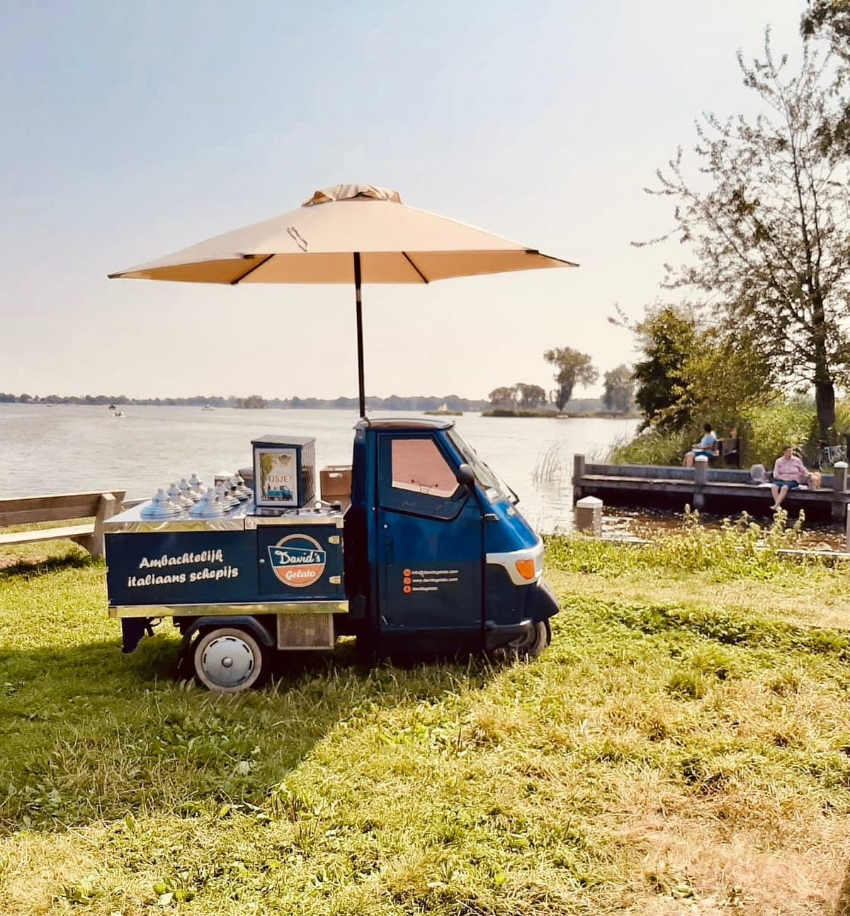 Mobile gelato cart by lakeside with umbrella serving customers