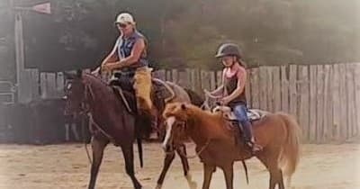 Parent and child riding horses together in rustic outdoor arena