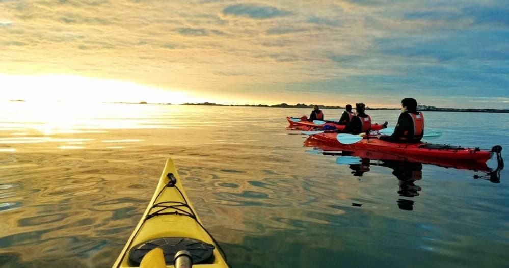 Paddlers kayaking at golden sunset with leading bow perspective