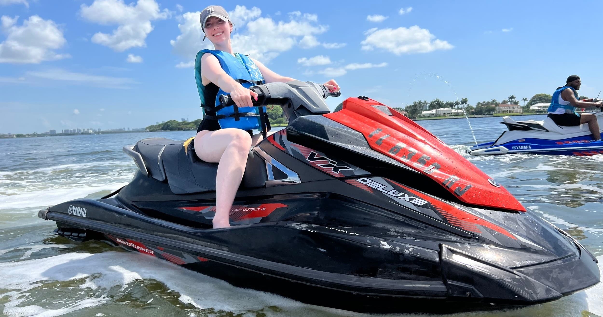 Rider on red jet ski speeding across coastal bay under sun
