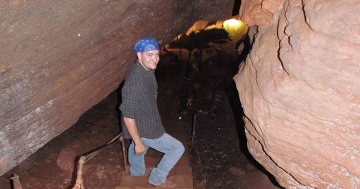 Explorer wearing helmet walking through narrow sandstone cave passage