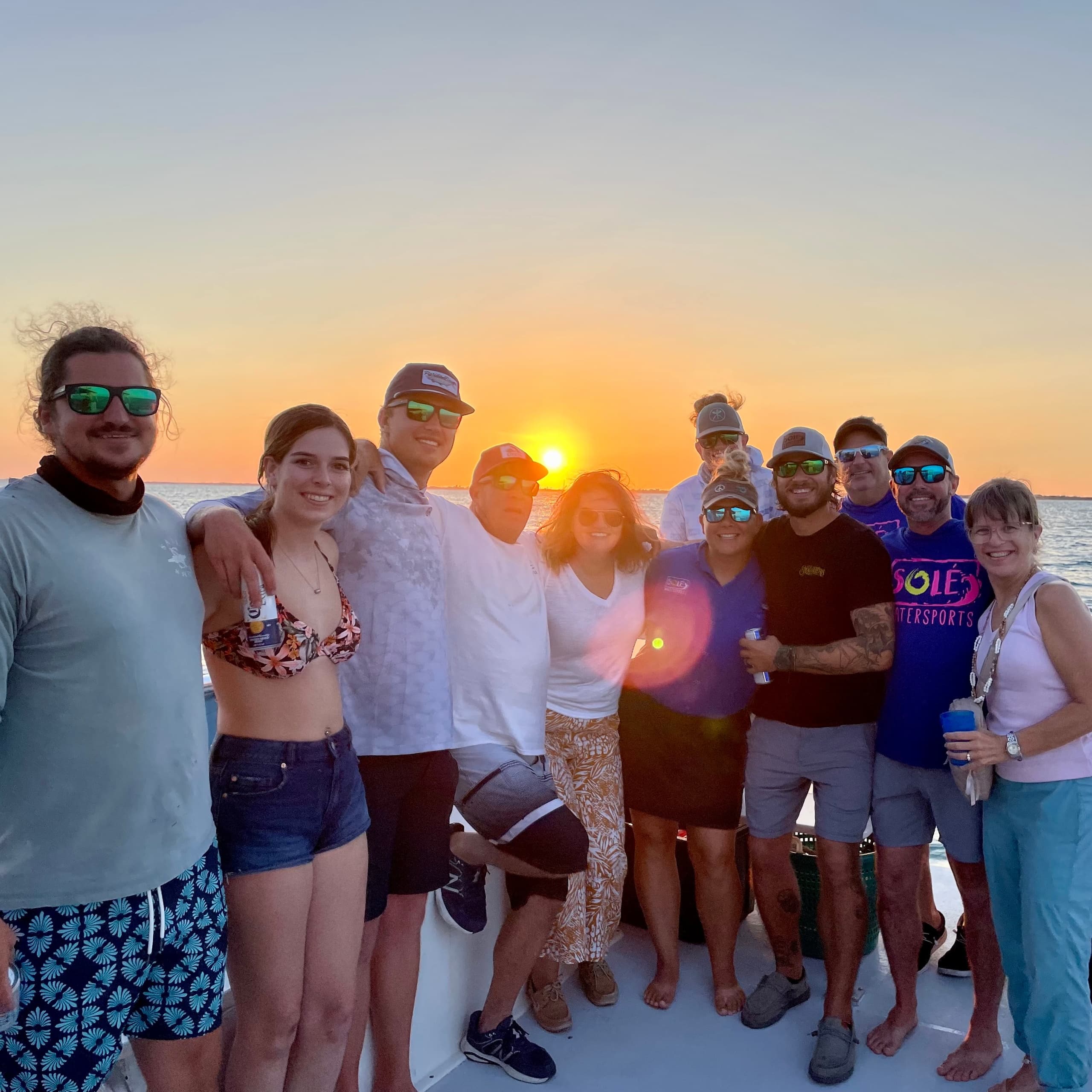 Friends posing on sunset boat cruise with golden horizon