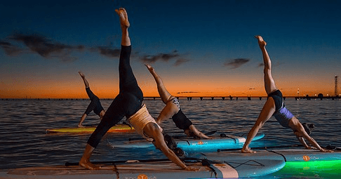 Sunset paddleboard yoga silhouettes on calm ocean