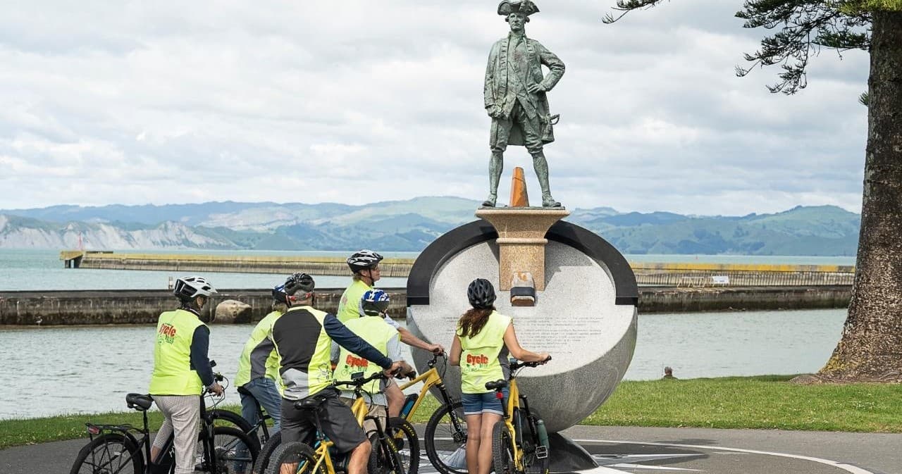 Cyclists in high-visibility vests gathered near waterfront statue