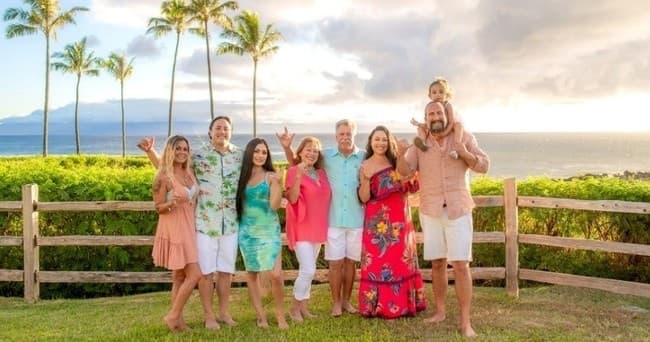 Extended family smiling by palms overlooking ocean at sunset
