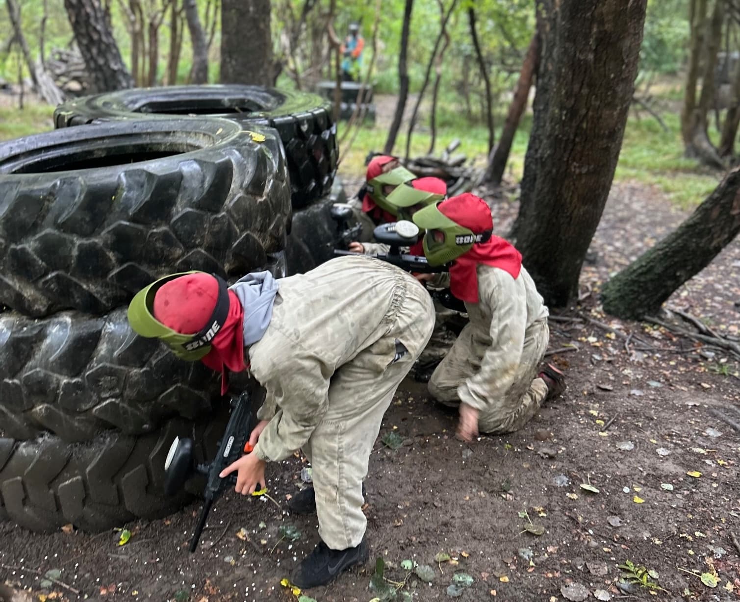 Young players crouching behind giant tyres during woodland paintball game