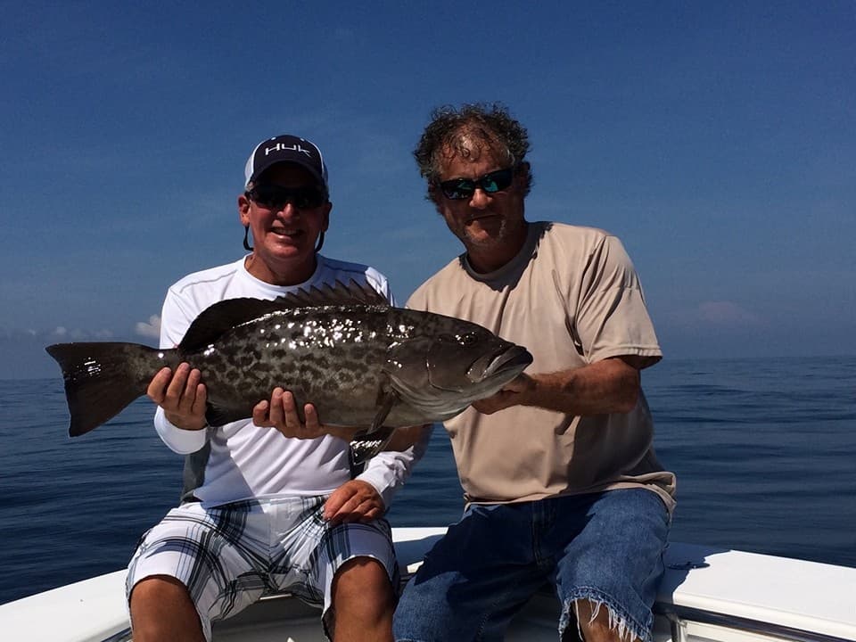 Anglers holding large grouper on sportfishing boat in Gulf