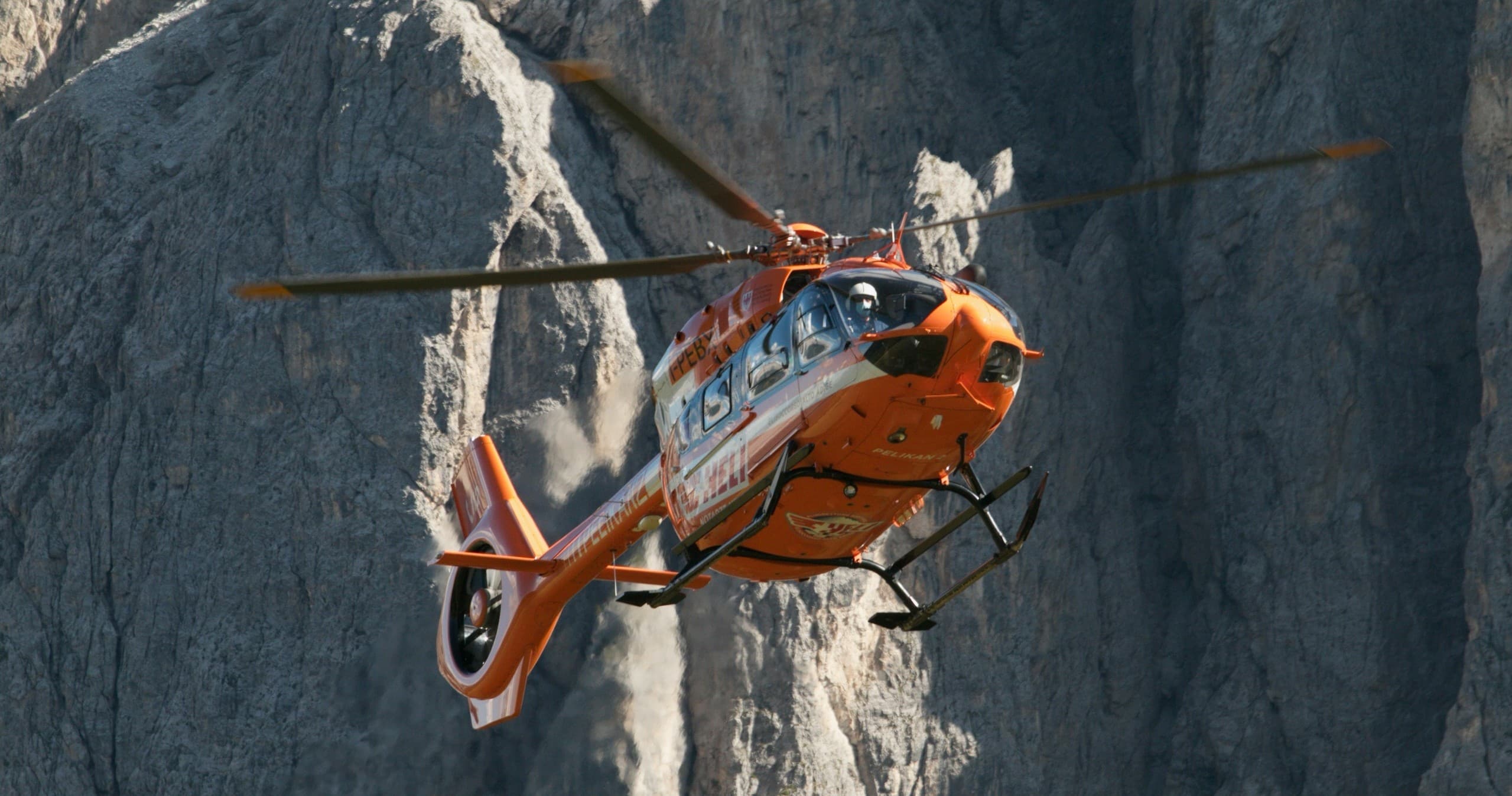 Orange helicopter flying along dramatic coastal rock cliffs