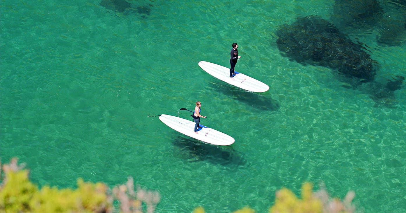 Aerial view of two paddleboarders on clear green bay waters