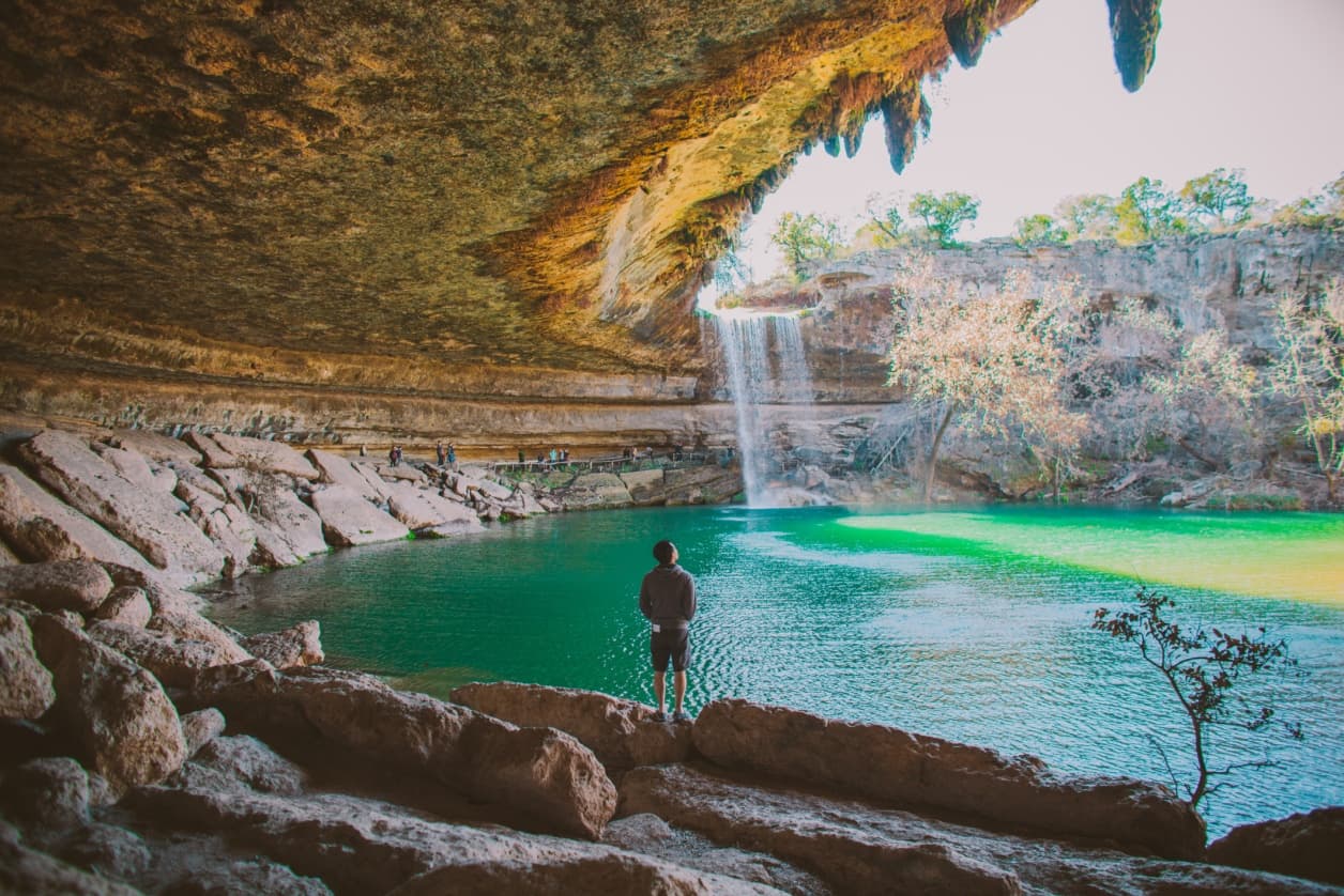 Hiker standing by turquoise waterfall pool in rocky grotto