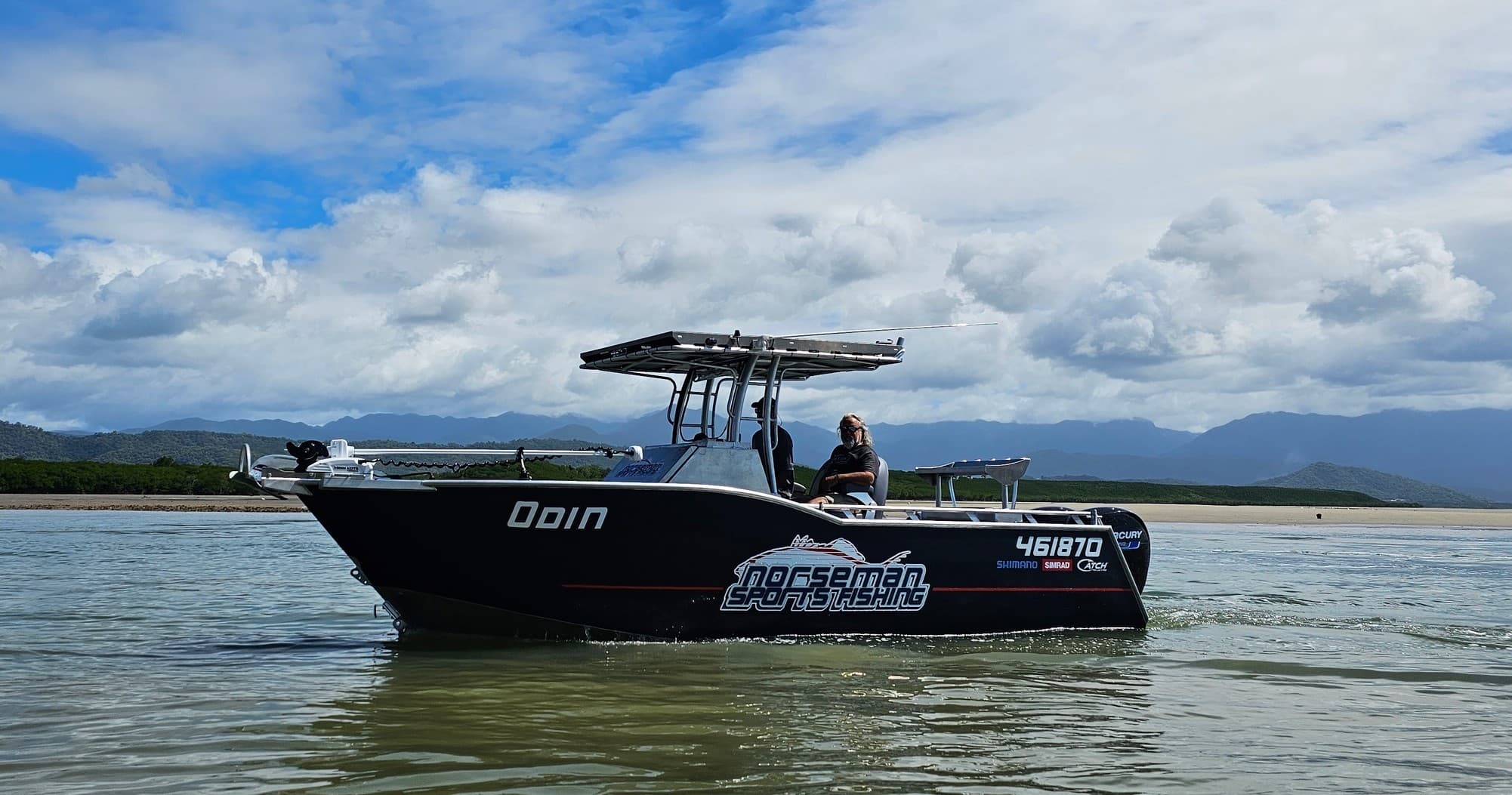 Black charter boat on calm coastal water with cloudy sky