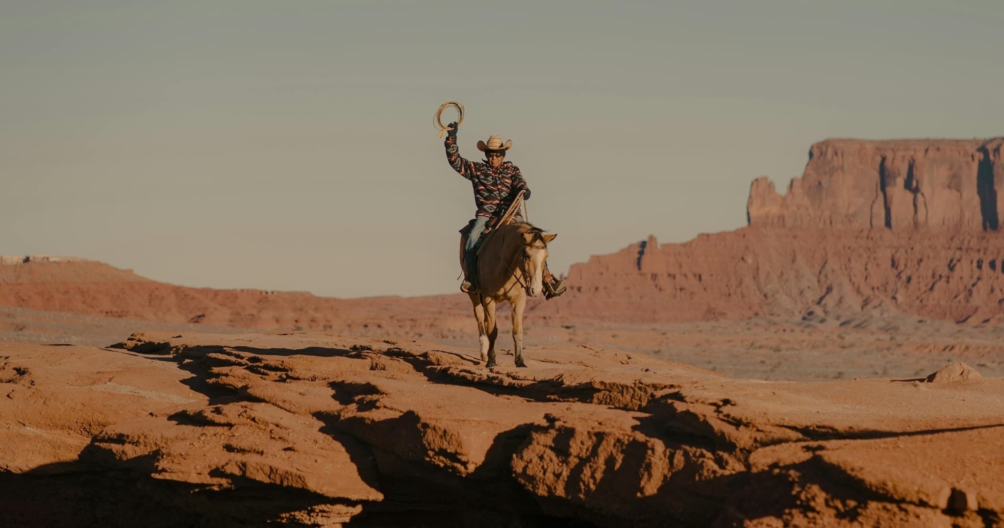 Cowboy riding across desert plateau with sandstone mesas