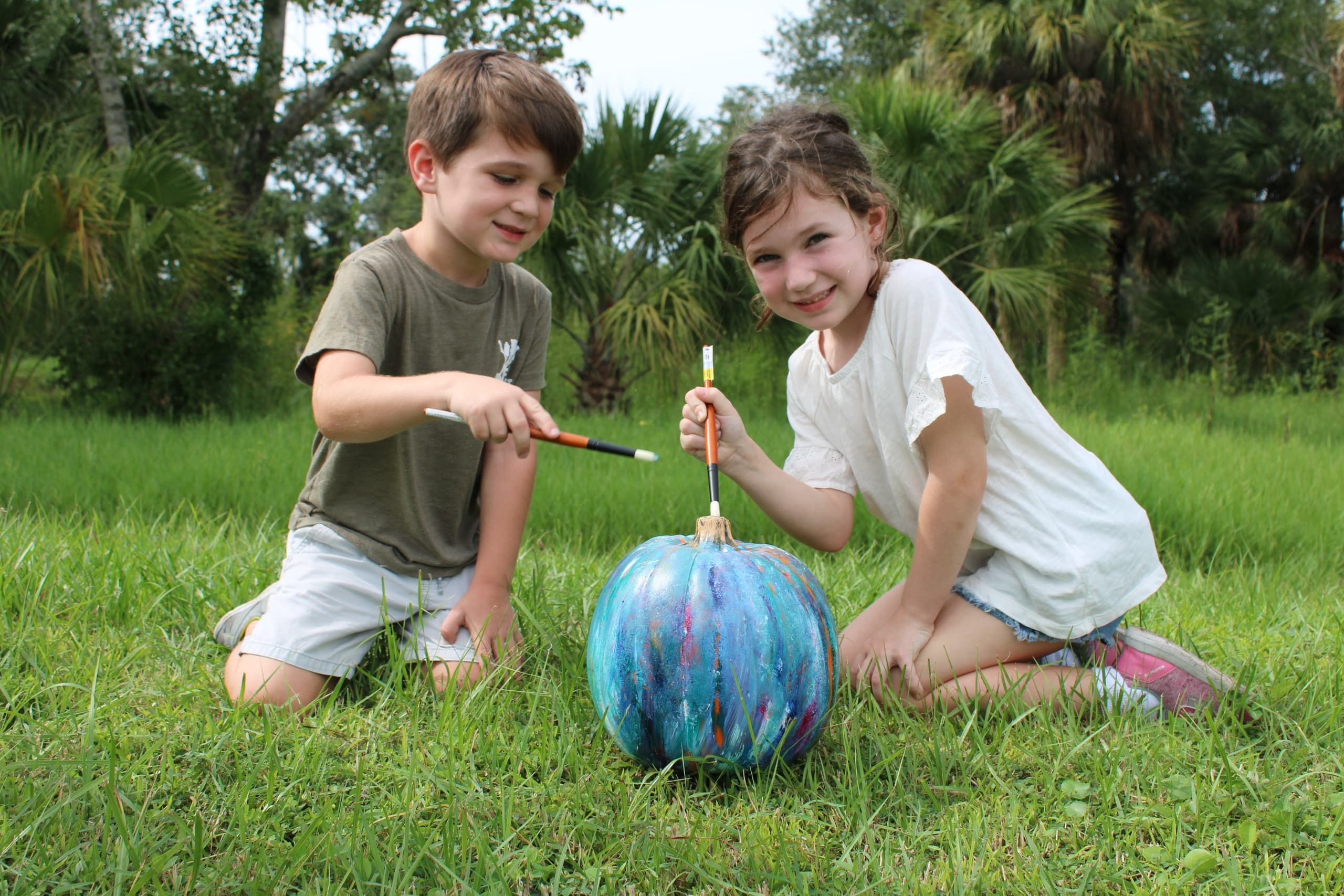 Children painting a colorful pumpkin on grass at farm