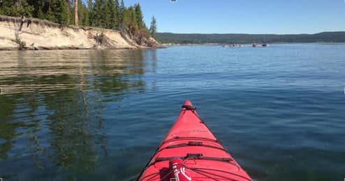 Kayak bow perspective paddling on calm lake with cliffs