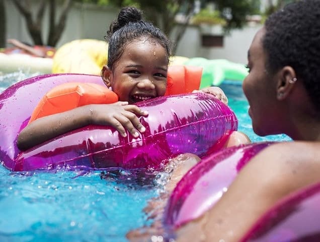 Children laughing on colorful pool floats in backyard pool