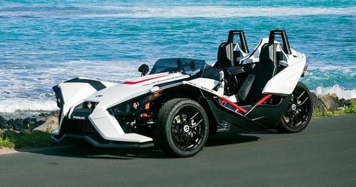 White slingshot parked along ocean coastal road, scenic view