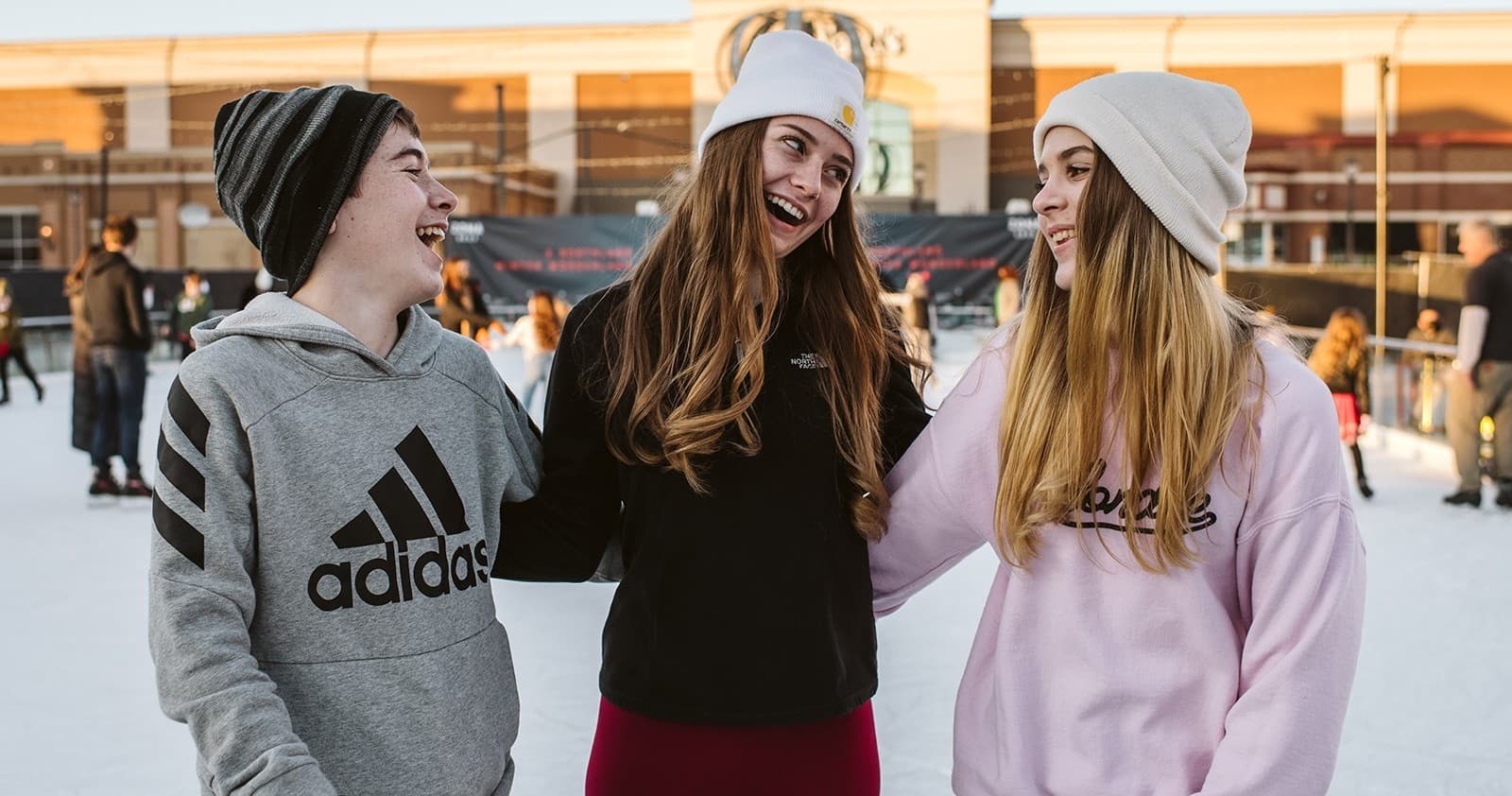 Three friends smiling on outdoor ice rink at sunset plaza