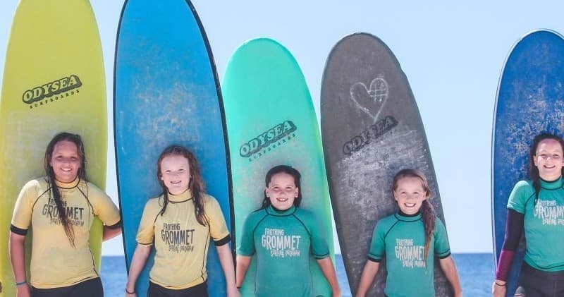 Kids in surf shirts posing with colorful surfboards on beach