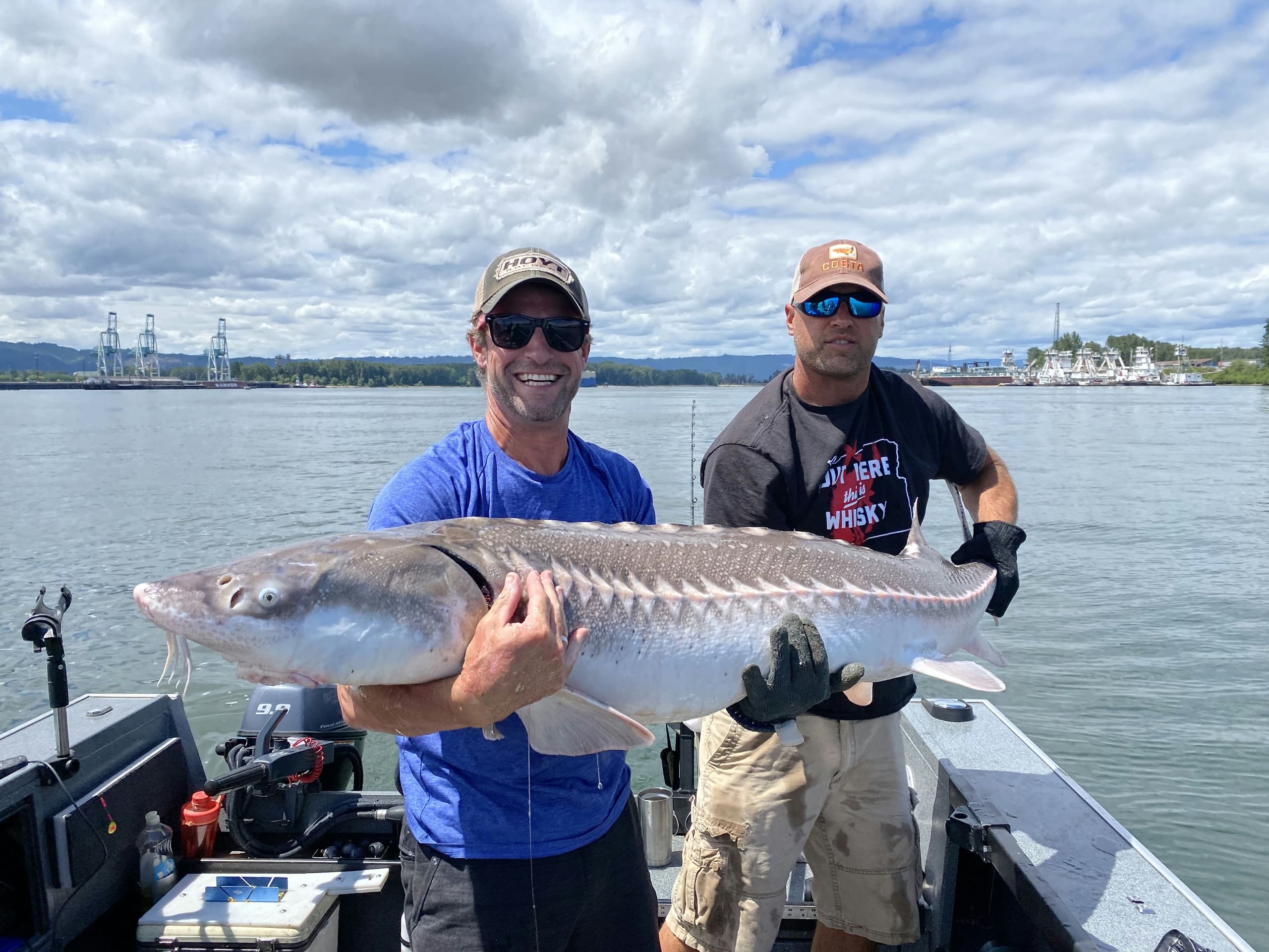 Two anglers holding large sturgeon aboard boat on estuary