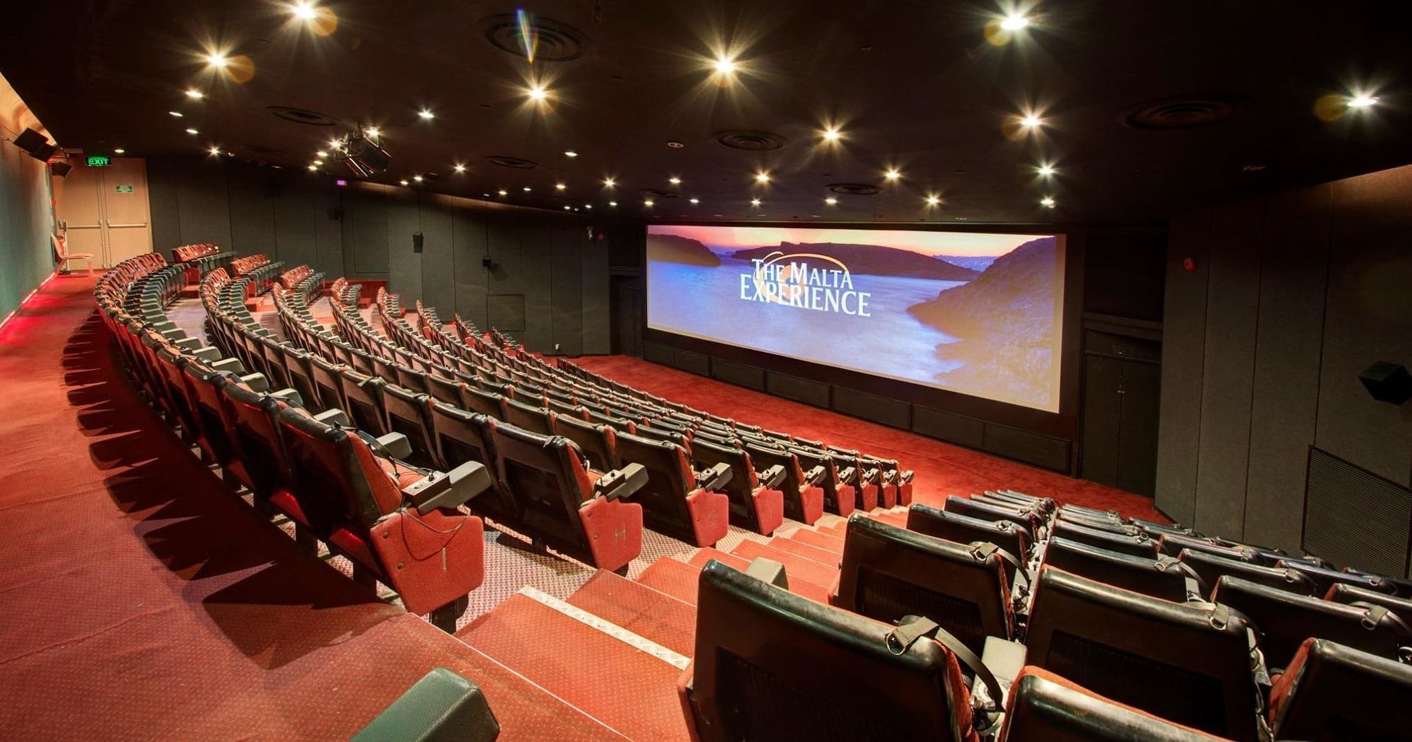 Indoor cinema theater screening with tiered red seats and screen
