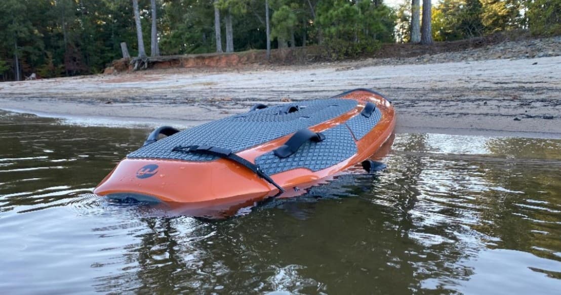 Orange electric surfboard on shallow lake shore at sunset