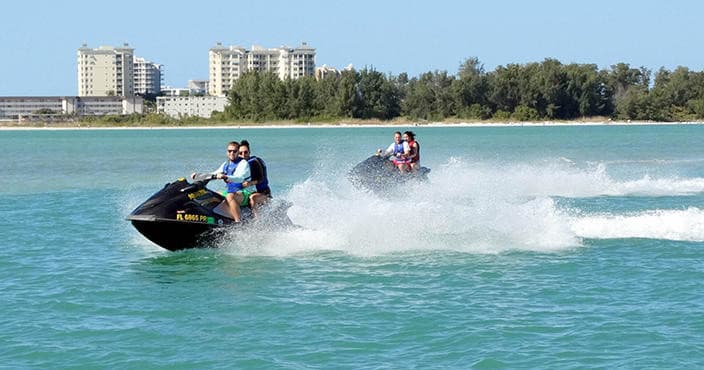 Two jet skis racing across turquoise bay with shoreline skyline