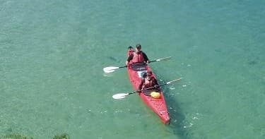 Two-person red kayak paddling on clear turquoise coastal bay