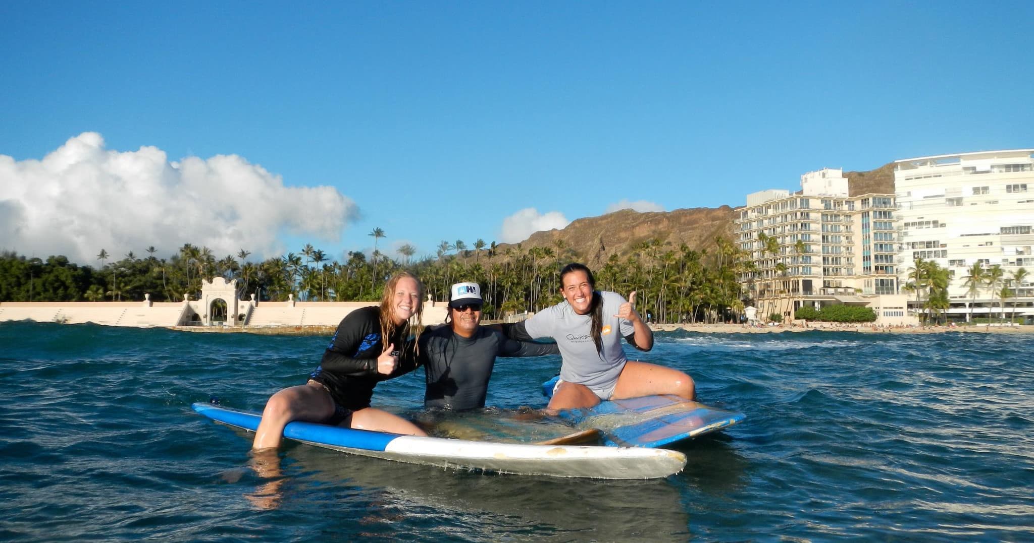 Three friends paddleboarding near sandy beach and palm-lined coast