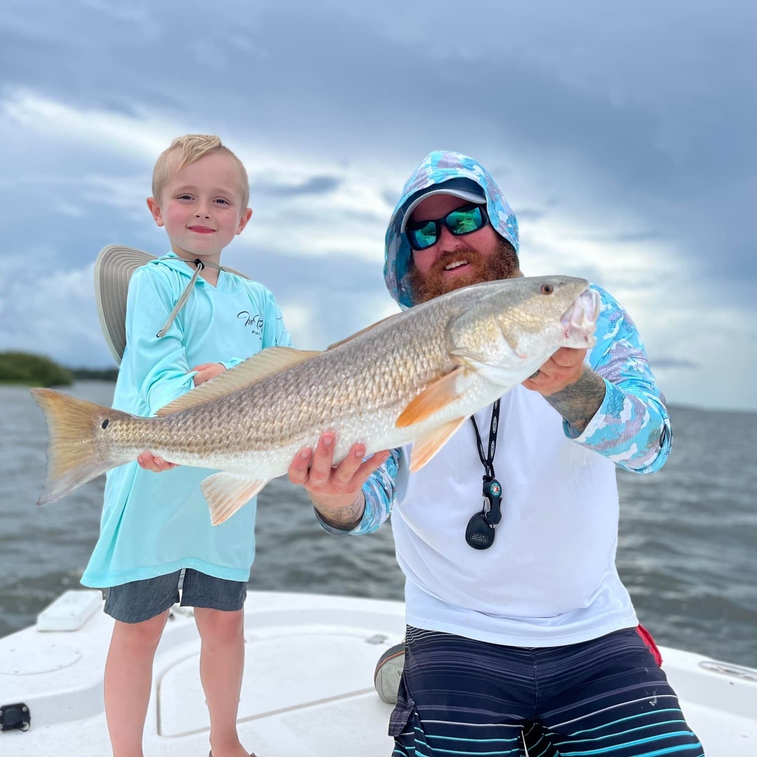 Guide and child holding trophy redfish on bow of charter fishing boat
