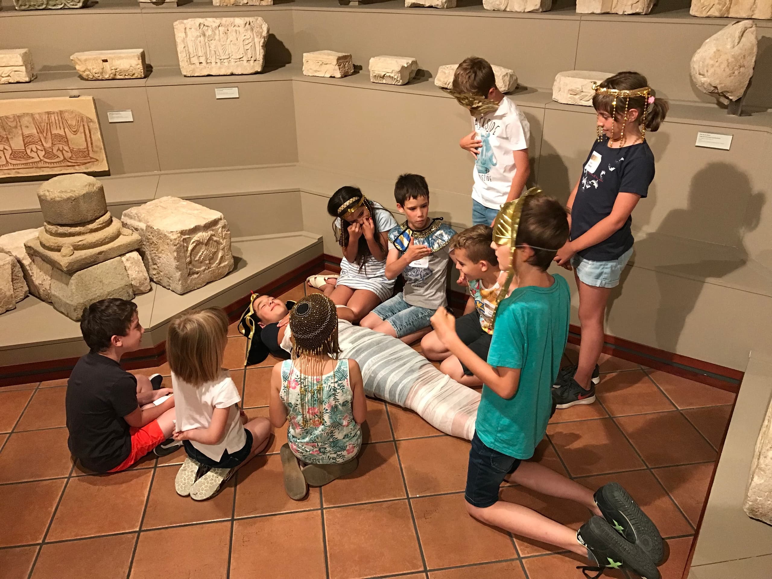 Children gathered around mummy exhibit on museum floor, learning