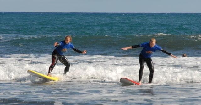 Two surfers riding small waves off Madeira coast, side-by-side