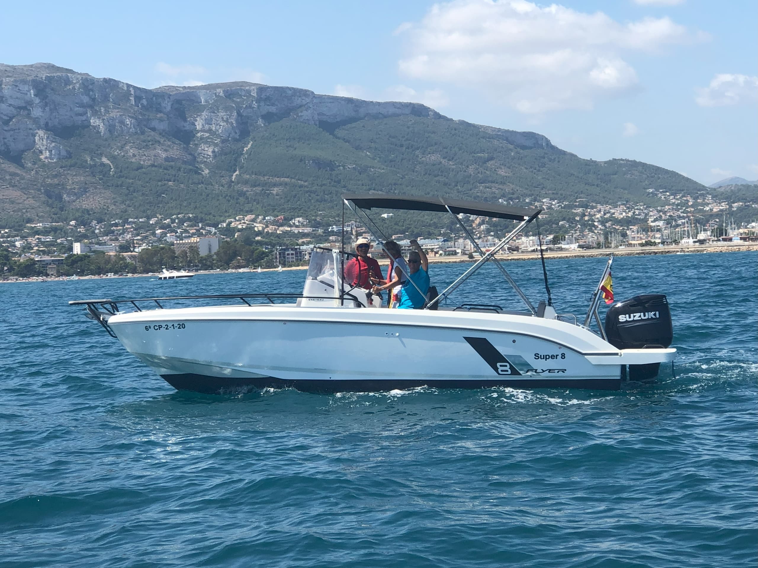 Family motorboat cruising near coastal hills and clear blue water