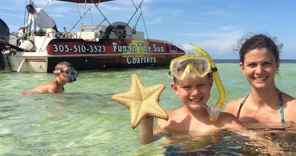 Family snorkeling in shallow clear water holding starfish in Key West