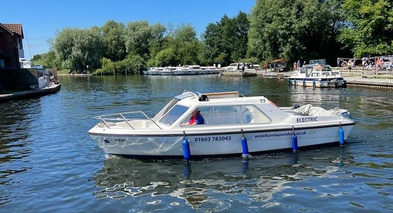 White cabin launch gliding across calm river with tree backdrop