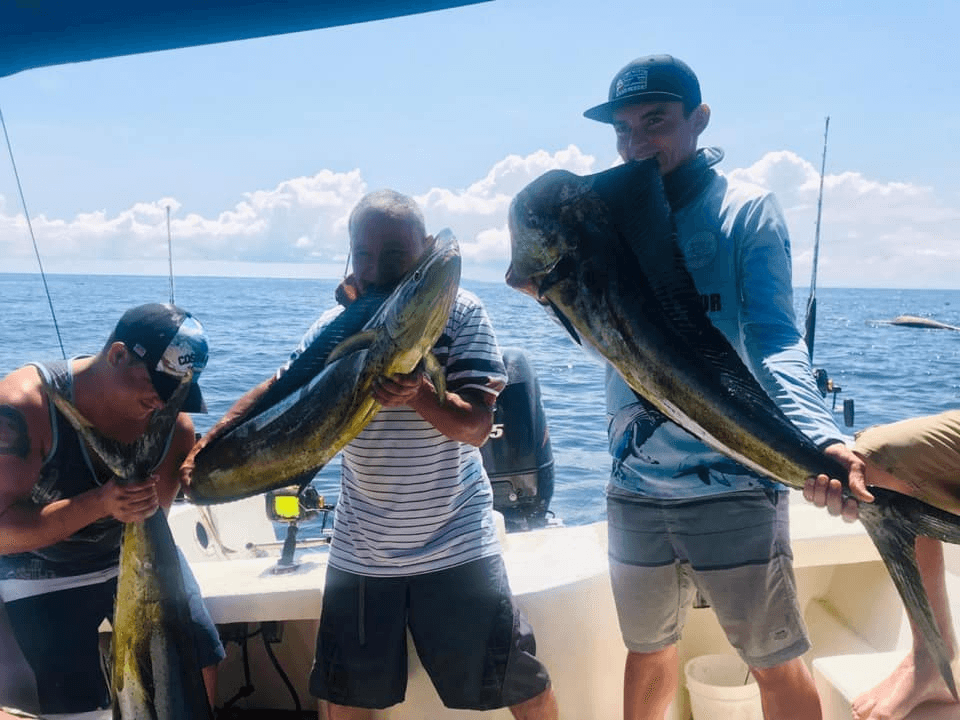 Group holding large mahi mahi catches aboard tropical fishing boat