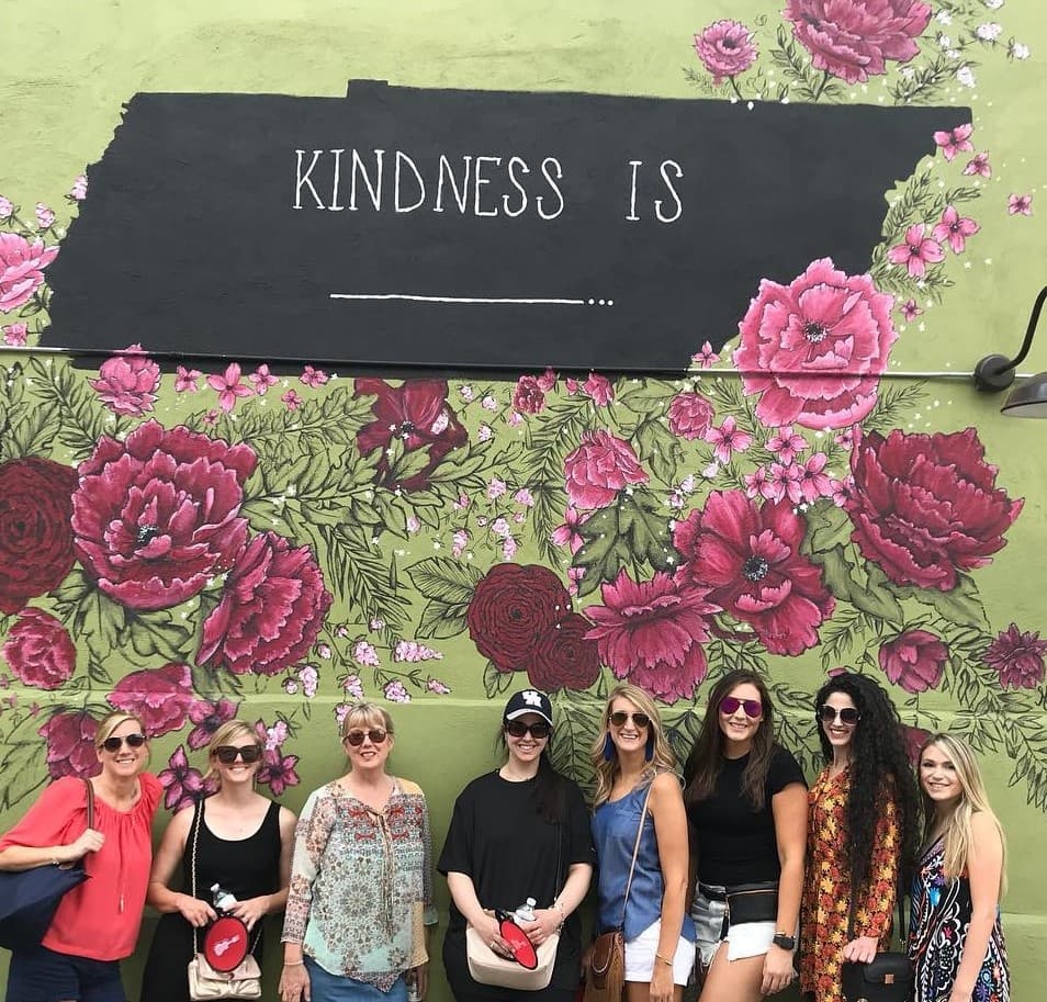 Group posing before 'Kindness Is' floral mural outdoors Nashville